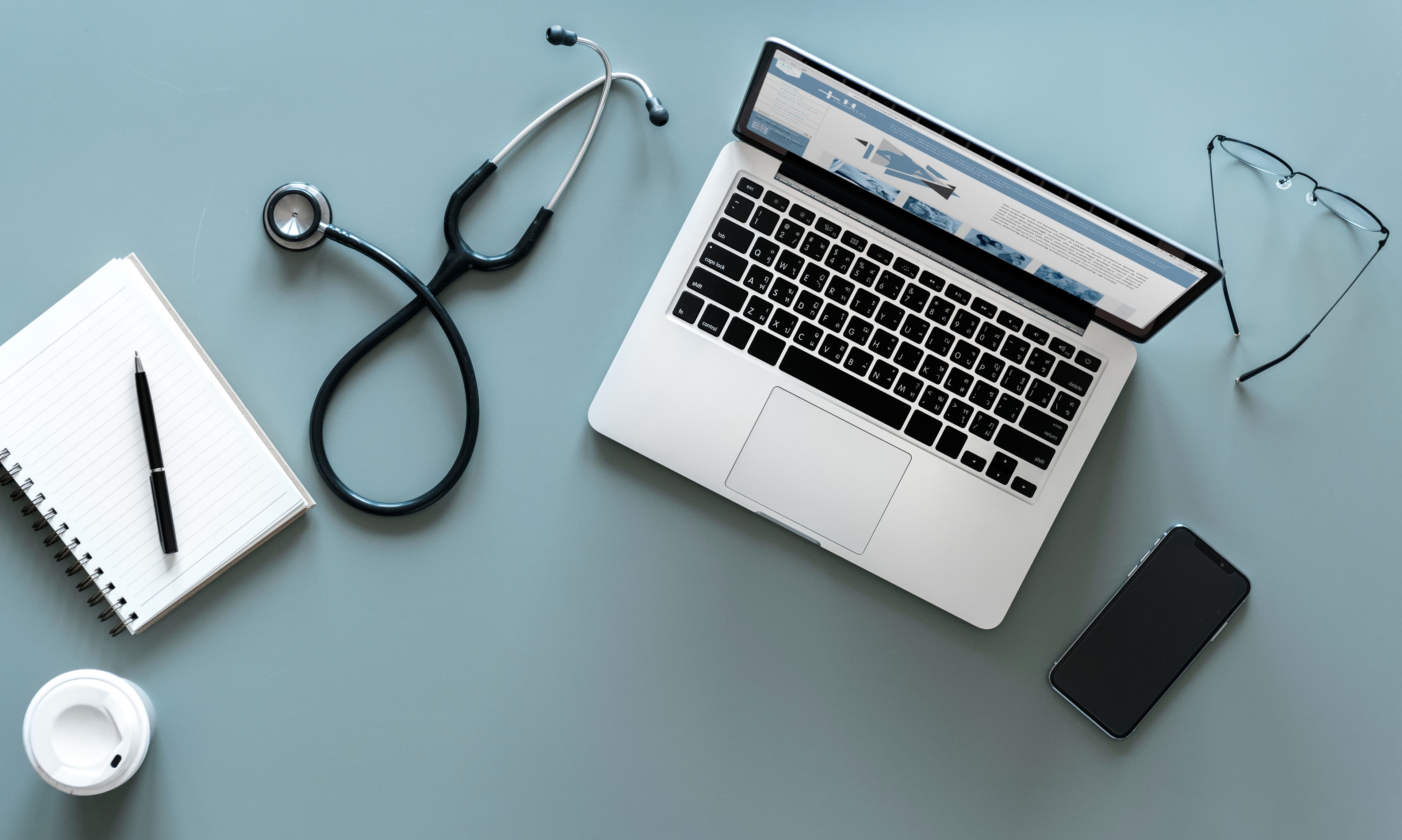 Laptop, stethoscope, glasses, and notebook on a desk